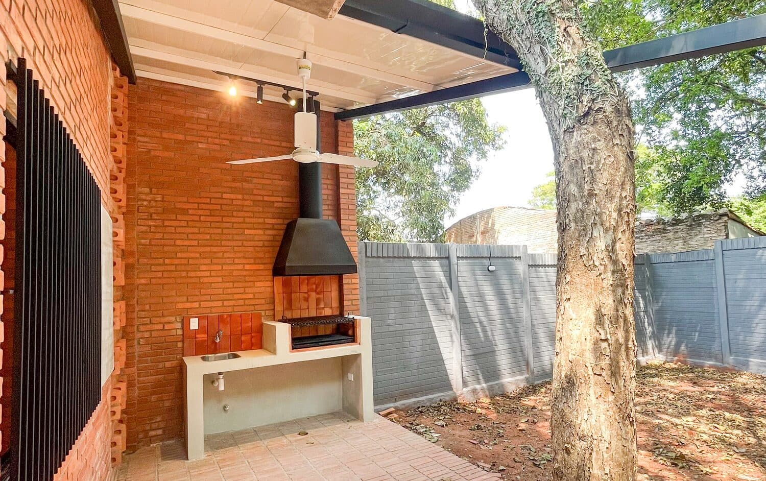 La galería techada con la parrilla y el árbol del terreno al borde del alero
