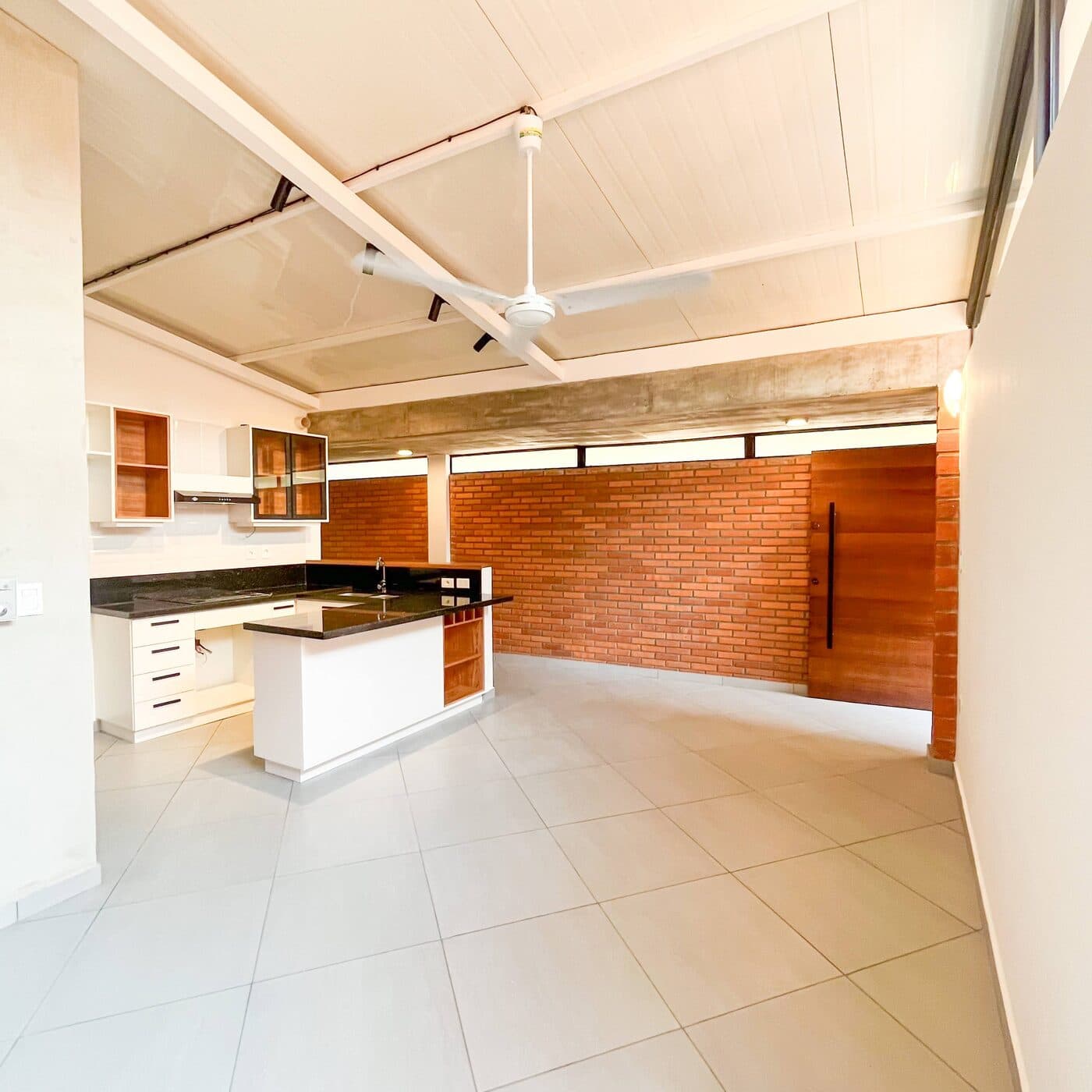 El estar y la cocina abiertos, con el muro de ladrillo visto y la puerta de madera al fondo