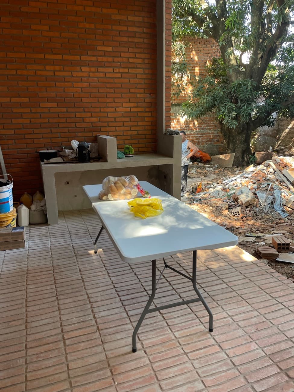 La mesa del asado sobre el piso de ladrillo del quincho, con alguien atendiendo la parrilla al fondo