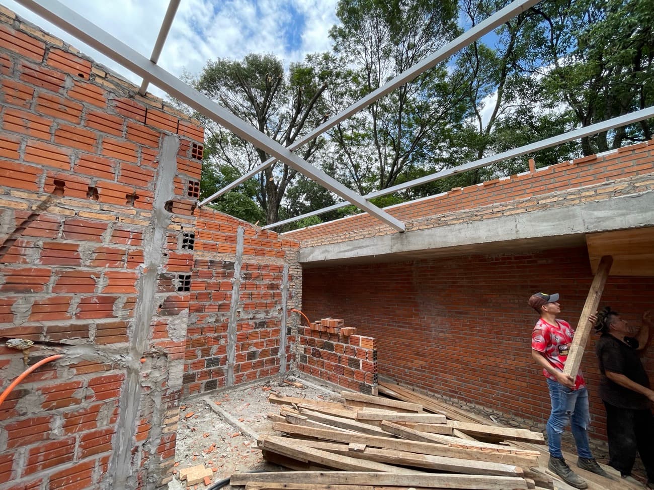 Dos operarios cargando un tirante bajo la estructura metálica del techo recién montada
