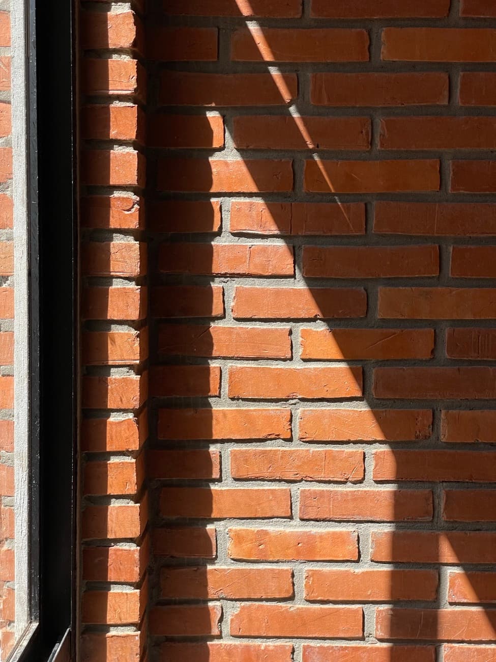 Una diagonal de sol cruzando el muro de ladrillo junto al marco negro de la ventana